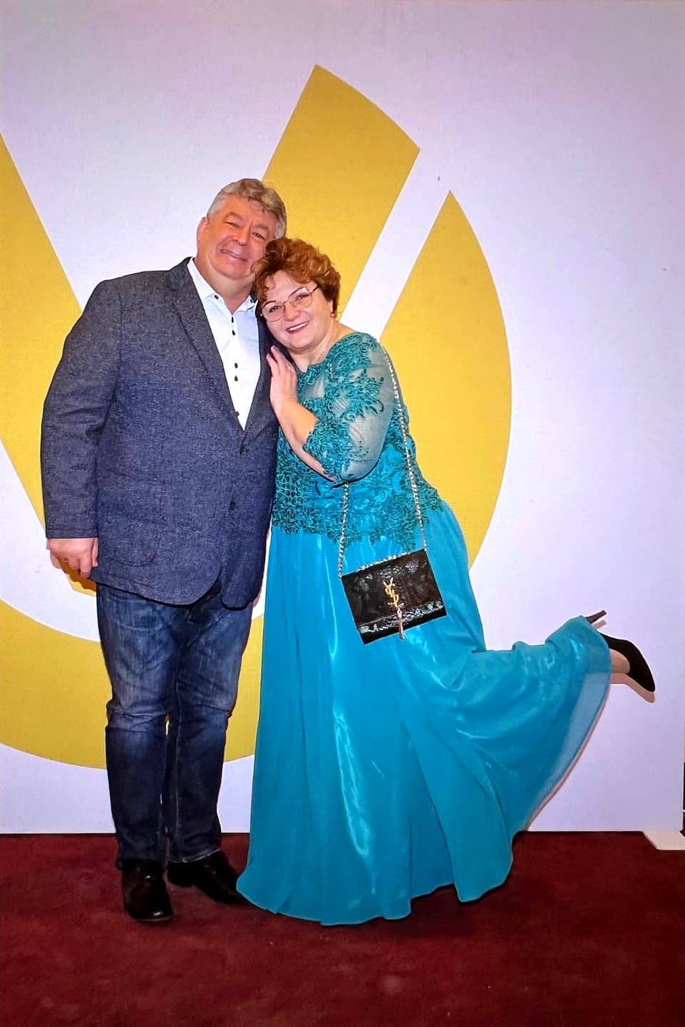 Larissa Etzel im türkisfarbenen Abendkleid lehnt sich lachend an einen Begleiter, dahinter das Logo der Deutschen Vermögensberatung.